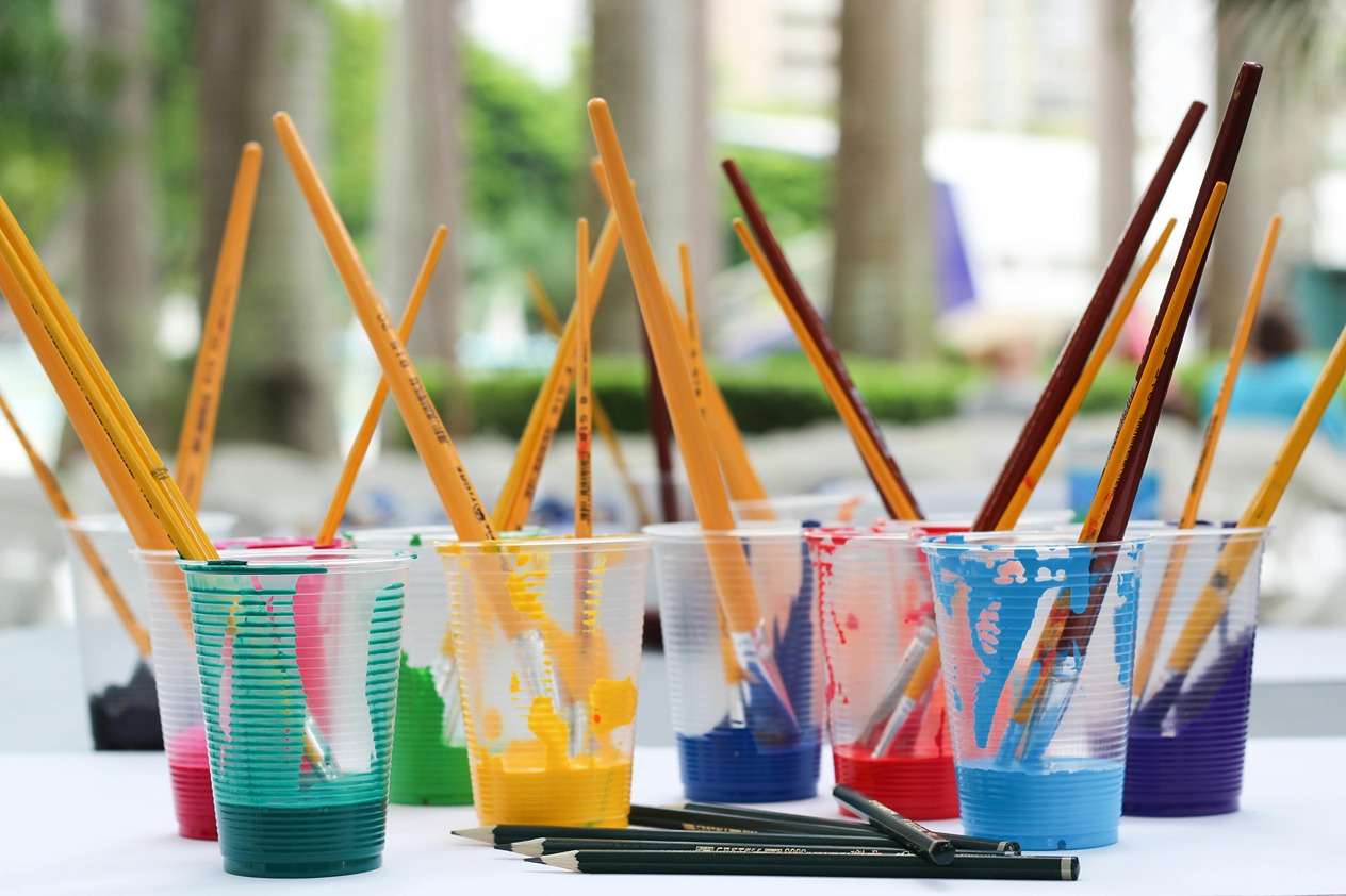 row of clear cups and filled with different colored paints and paintbrushes
