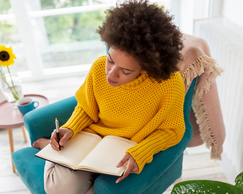 Black woman sitting on a chair writing in a journal